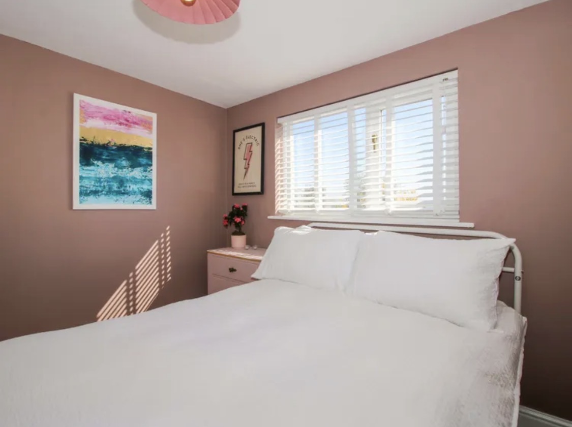 Pink bedroom walls beside a window with white blinds